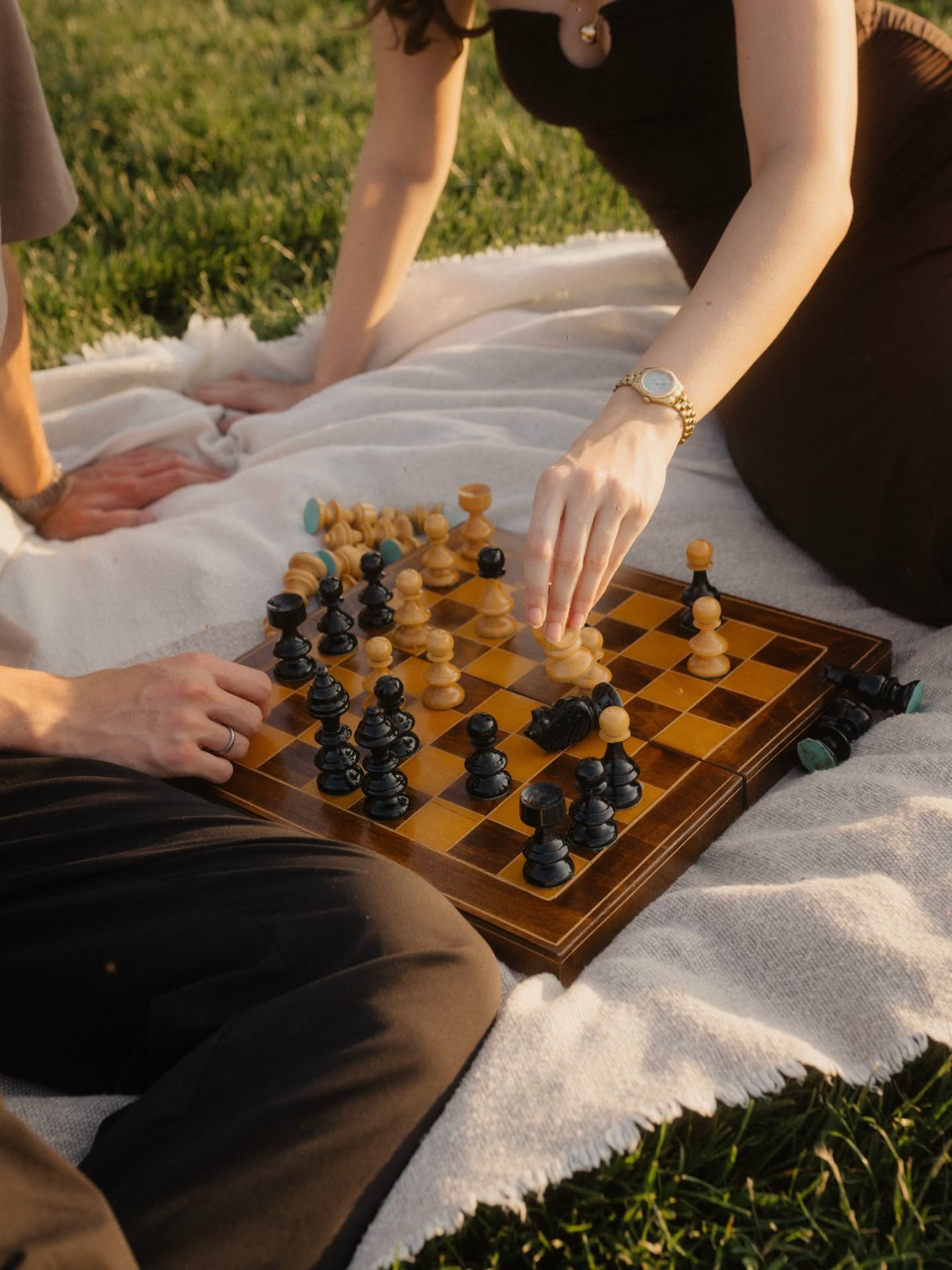 Friends gathered around a wooden chess set outdoors, playing together in the sun